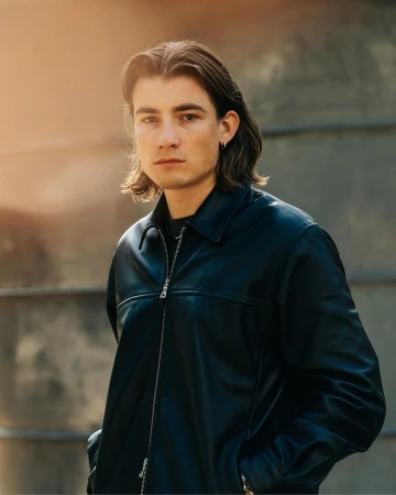 Portrait of a man with long brown hair wearing a dark leather jacket outdoors in New York by Adam Katz Sinding