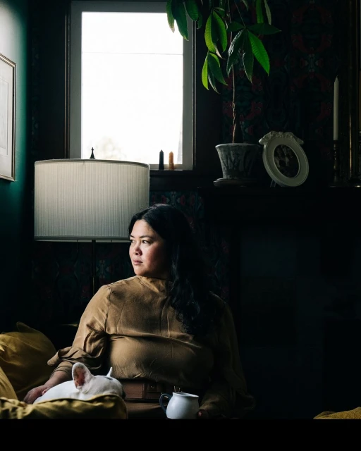 Adult woman lounges indoors with a white French Bulldog, a white coffee mug, and warm yellow lighting, creating a cozy, comfortable scene.