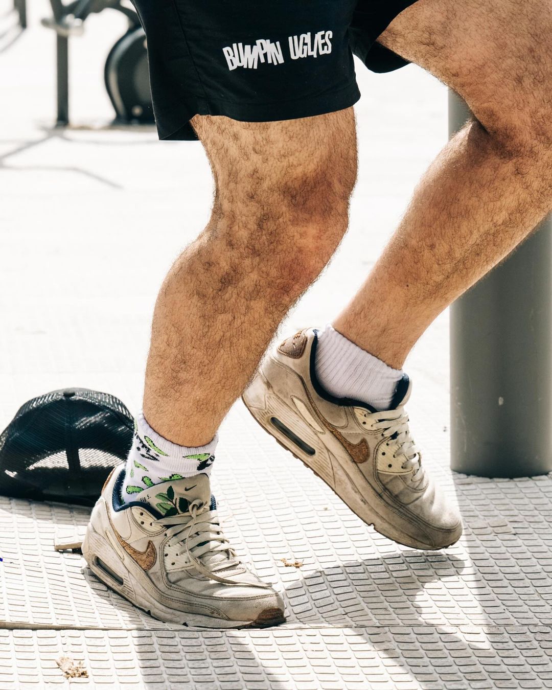 Close-up shot of a person's legs and feet wearing white sneakers with patterned socks. The person is wearing black shorts.