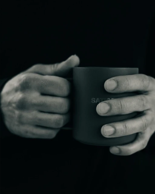 Close-up shot of hands holding a dark mug against a black backdrop, displaying a minimalist aesthetic and a sense of warmth.