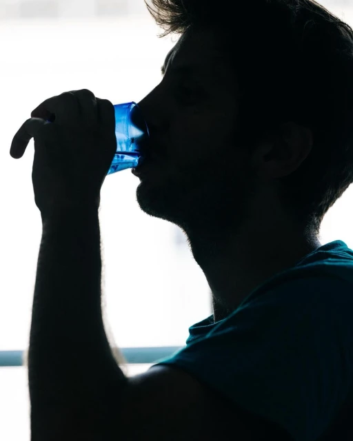 Silhouette of a man drinking water from a blue glass, side profile, bright window background, indoor setting, health and wellness.