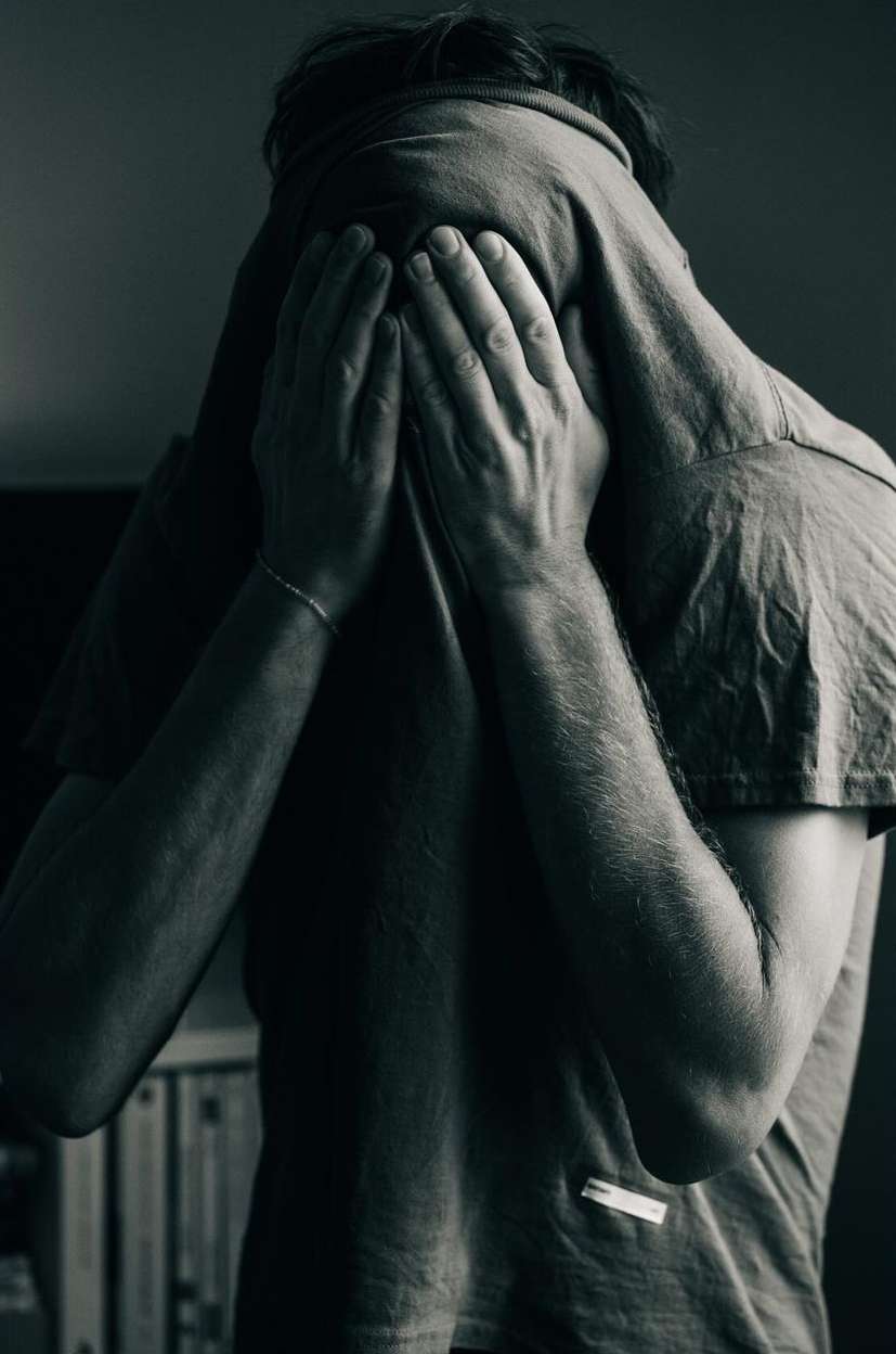 Monochrome portrait of a person pulling a t shirt over their face covering their eyes and hiding from the camera