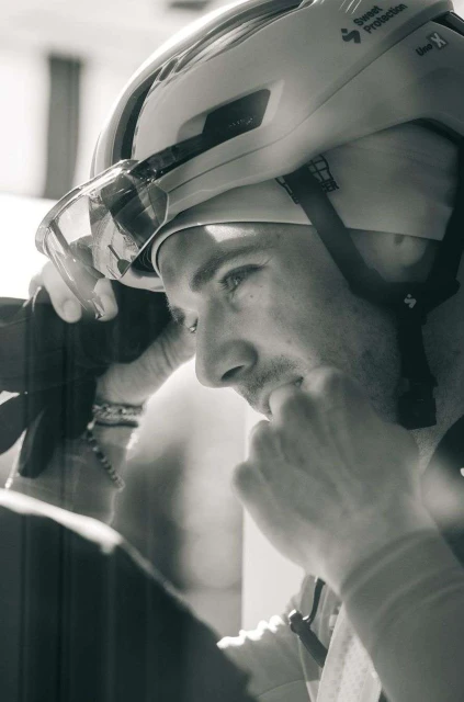 Monochrome portrait of a man wearing a cycling helmet with visor and adjusting the straps, indoor environment, close-up framing.