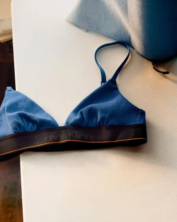 Blue Calvin Klein bra on a white surface, featuring a ribbed texture and black band with brand logo, complemented by a light blue backdrop.