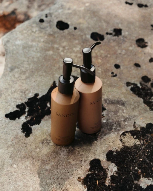 Two tan pump bottles with black pumps stand on a textured gray stone surface with dark spots, photographed in a product shot.
