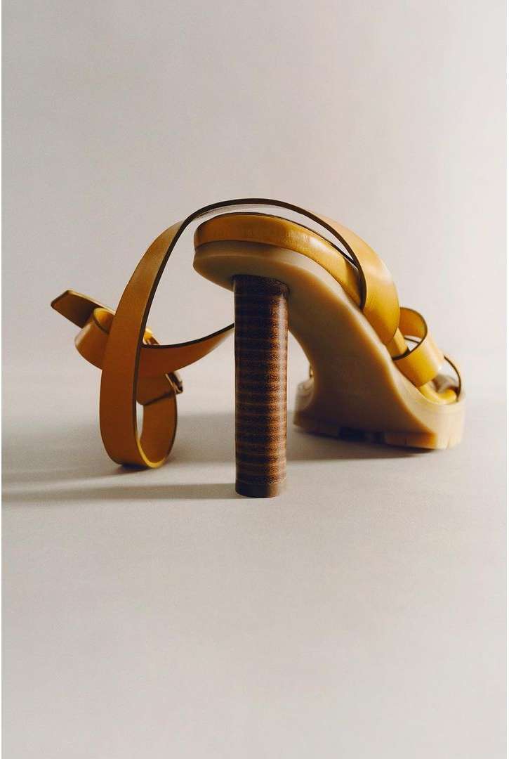 Elevated shot of an open-toe yellow sandal with thin straps and a cylindrical brown heel, set against a neutral background, showcasing fashion footwear.
