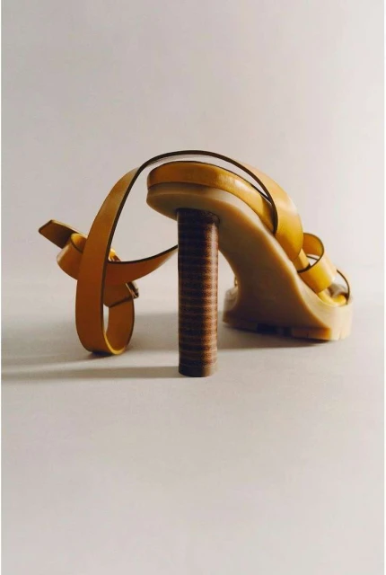 Elevated shot of an open-toe yellow sandal with thin straps and a cylindrical brown heel, set against a neutral background, showcasing fashion footwear.