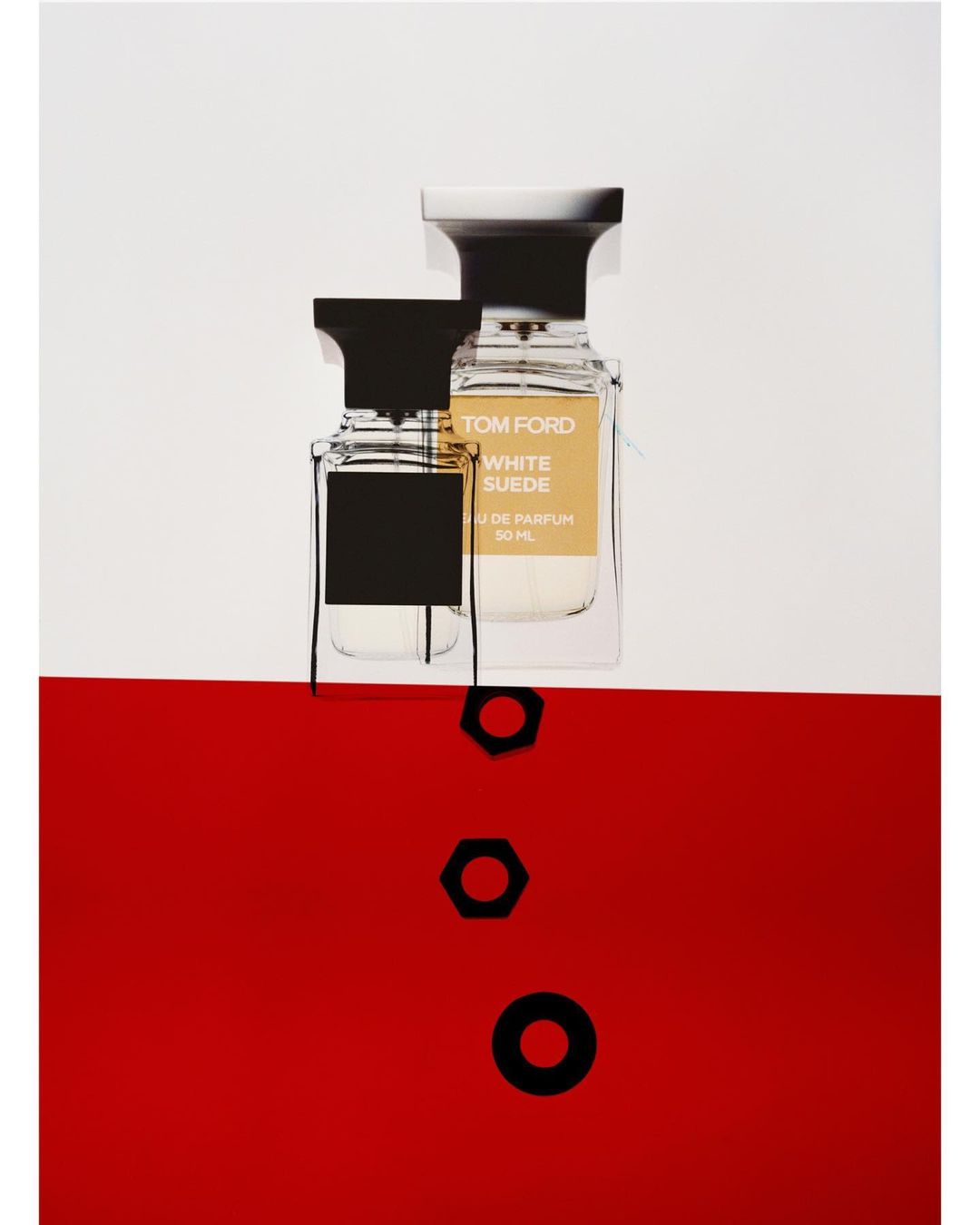 Tom Ford White Suede perfume bottles on a two-tone white and red background with geometric black accents in a studio setting.