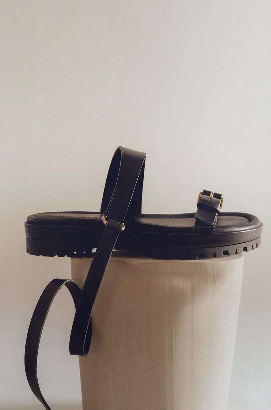Brown leather platform sandals showcased on a white cylindrical pedestal against a plain background in a studio setting.