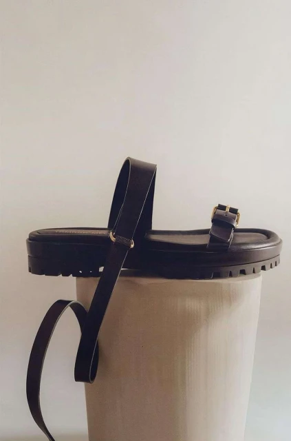 Brown leather platform sandals showcased on a white cylindrical pedestal against a plain background in a studio setting.