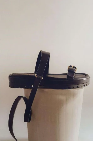 Brown leather platform sandals showcased on a white cylindrical pedestal against a plain background in a studio setting.