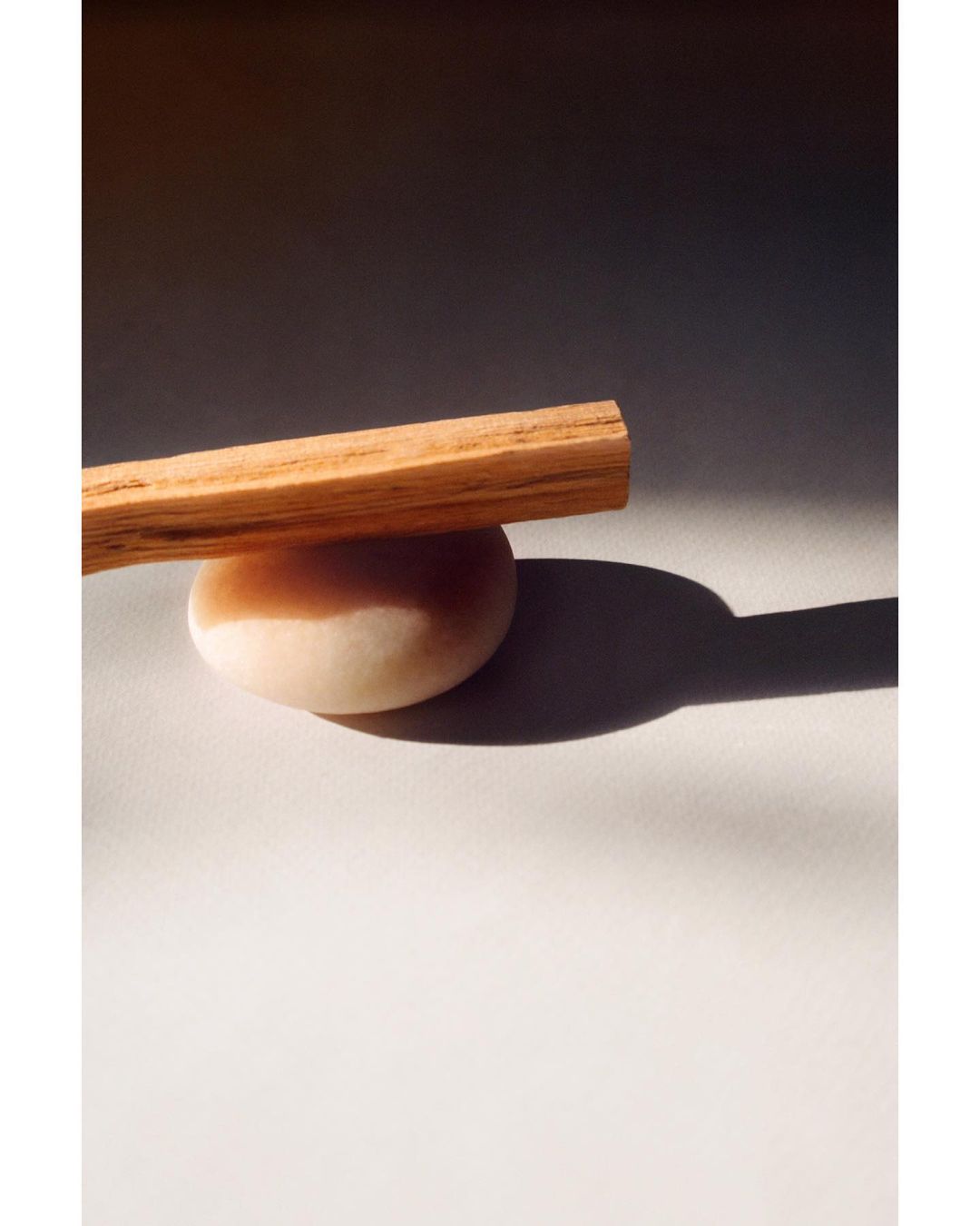 Palo santo stick resting on a round stone against a grey and white background, illuminated by warm, natural lighting.
