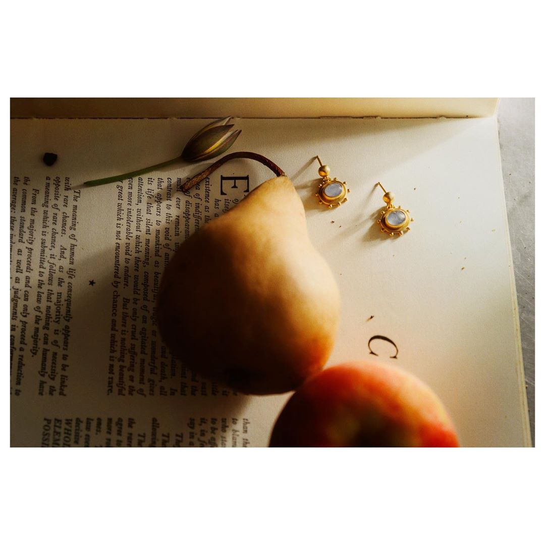 Still life featuring a pear, earrings, a peach, and a flower bud arranged on an open book with printed text.