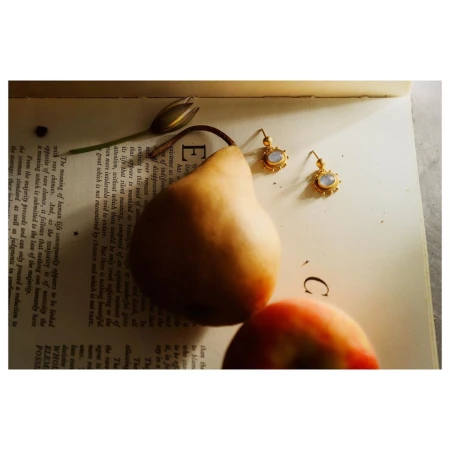 Still life featuring a pear, earrings, a peach, and a flower bud arranged on an open book with printed text.