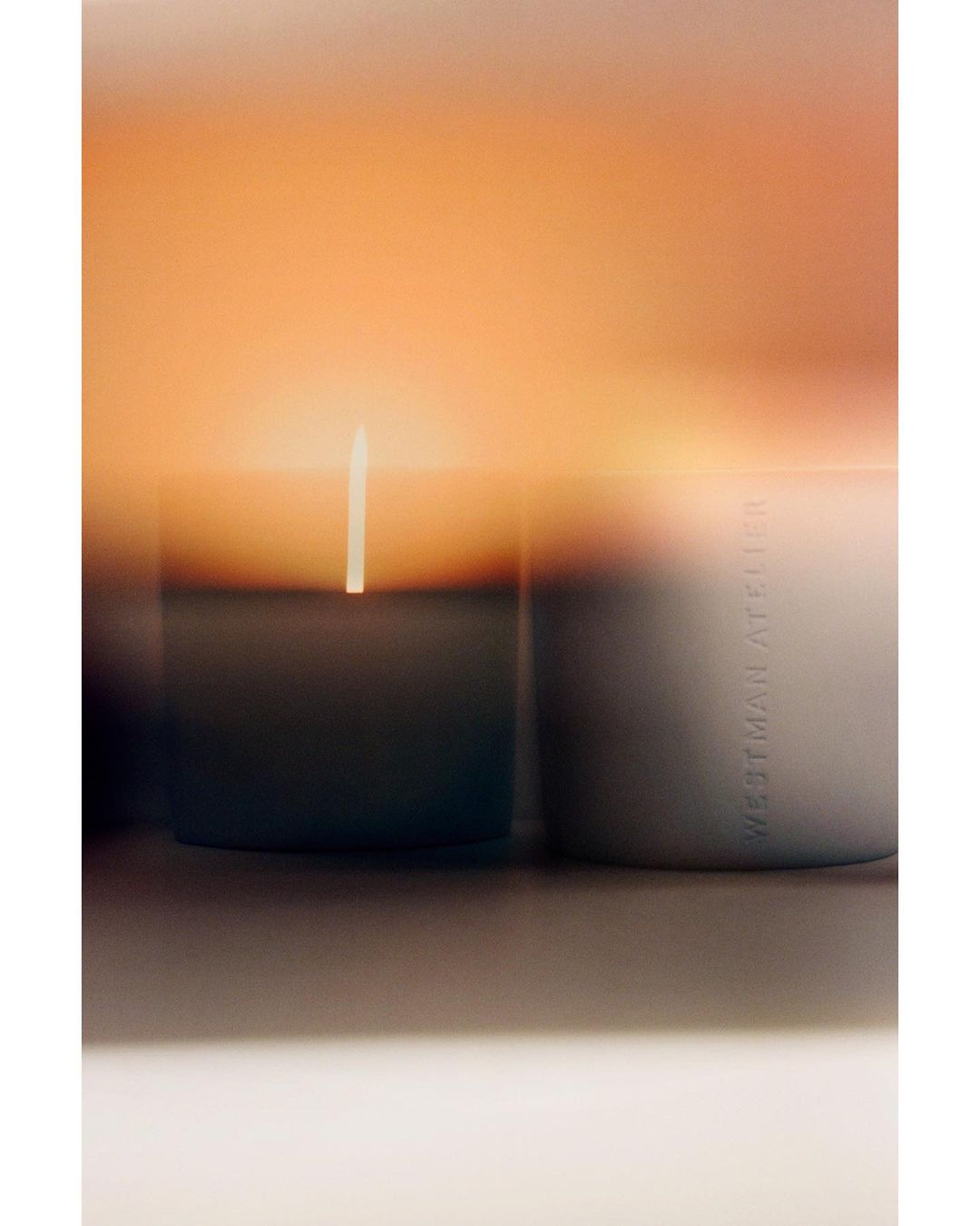 Close-up studio shot of a candle emitting light with the brand Westman Atelier visible on the side of the candle container.