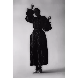 Black and white portrait of a woman in a patterned dress with puffed sleeves posing against a plain backdrop