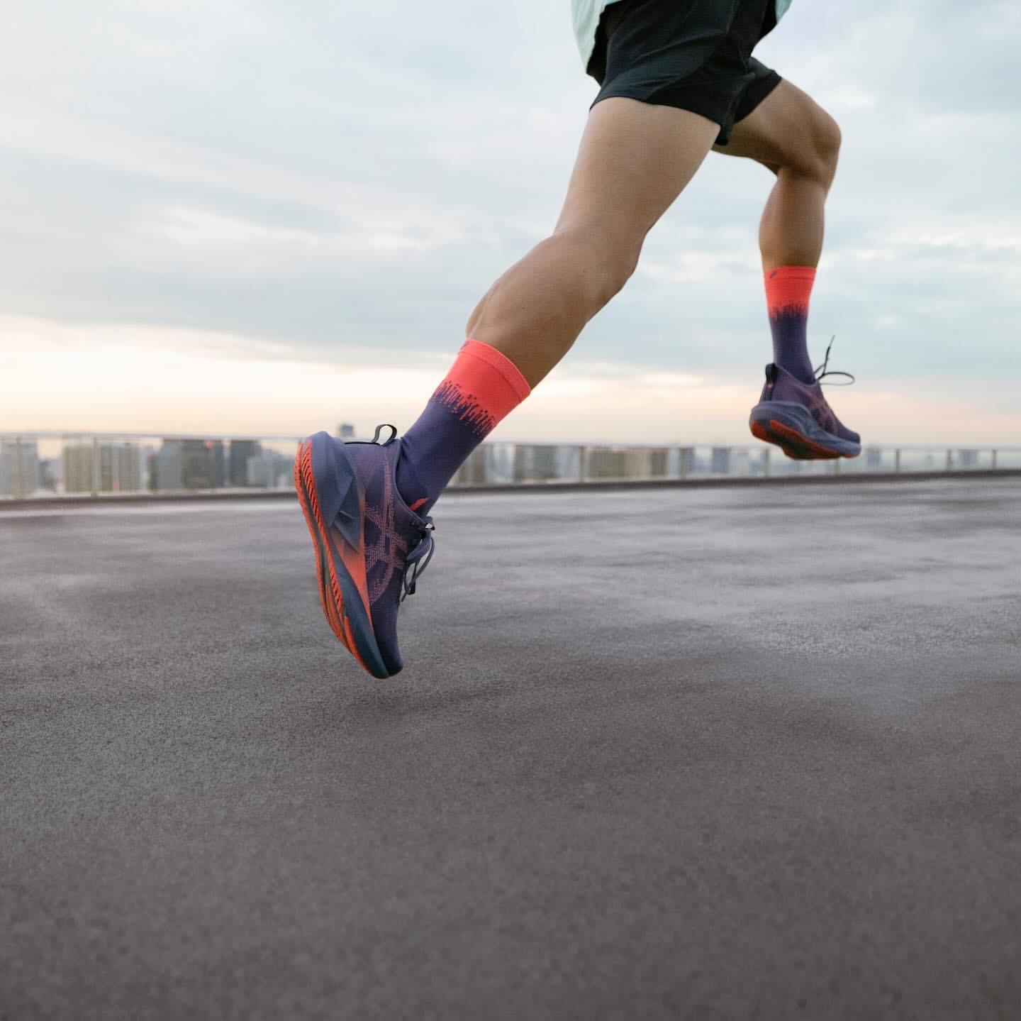 Close-up of a person running outdoors on a rooftop, showcasing athletic shoes and socks against an urban skyline at dusk.