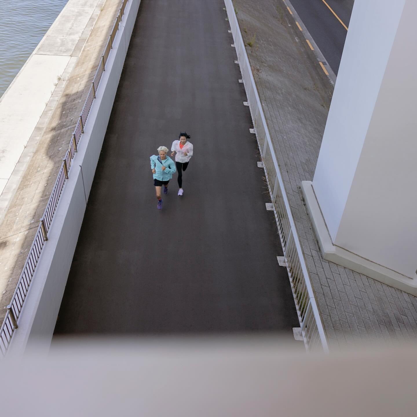 Two women jogging together on a paved path along the water on a sunny day. Healthy lifestyle and outdoor fitness concept.