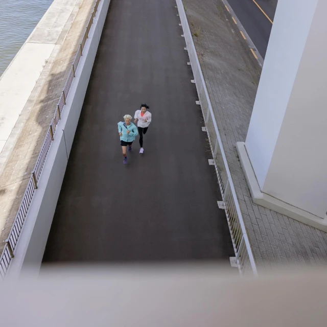 Two women jogging together on a paved path along the water on a sunny day. Healthy lifestyle and outdoor fitness concept.