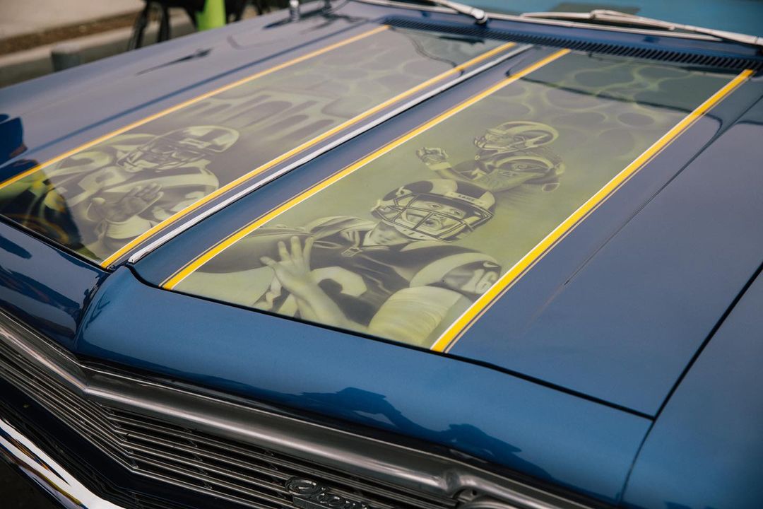 Custom blue car hood featuring airbrushed portraits of football players with helmets and yellow stripes creating a striking automotive artwork.