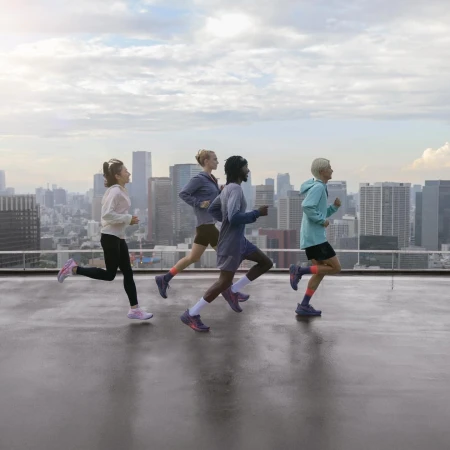 Four athletic women run on a rooftop overlooking a cityscape. They are wearing athletic wear and running shoes during a workout.