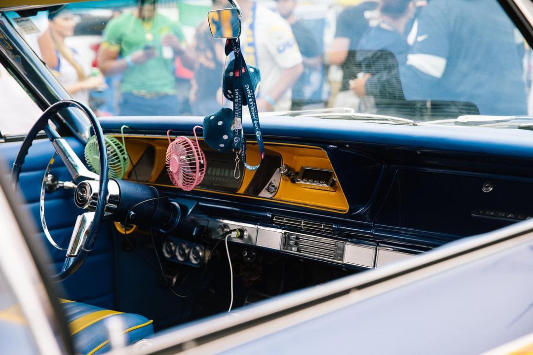 Classic car interior with blue and yellow accents, retro dashboard, steering wheel, fuzzy dice, and miniature fans on display.