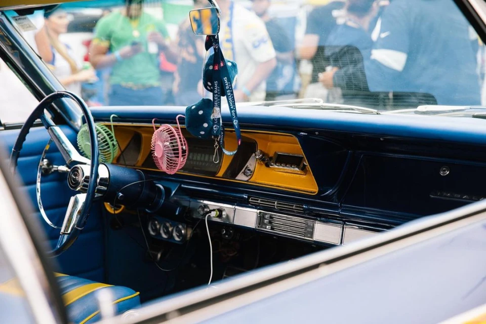 Classic car interior with blue and yellow accents, retro dashboard, steering wheel, fuzzy dice, and miniature fans on display.