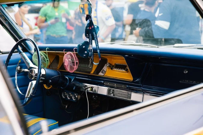 Classic car interior with blue and yellow accents, retro dashboard, steering wheel, fuzzy dice, and miniature fans on display.
