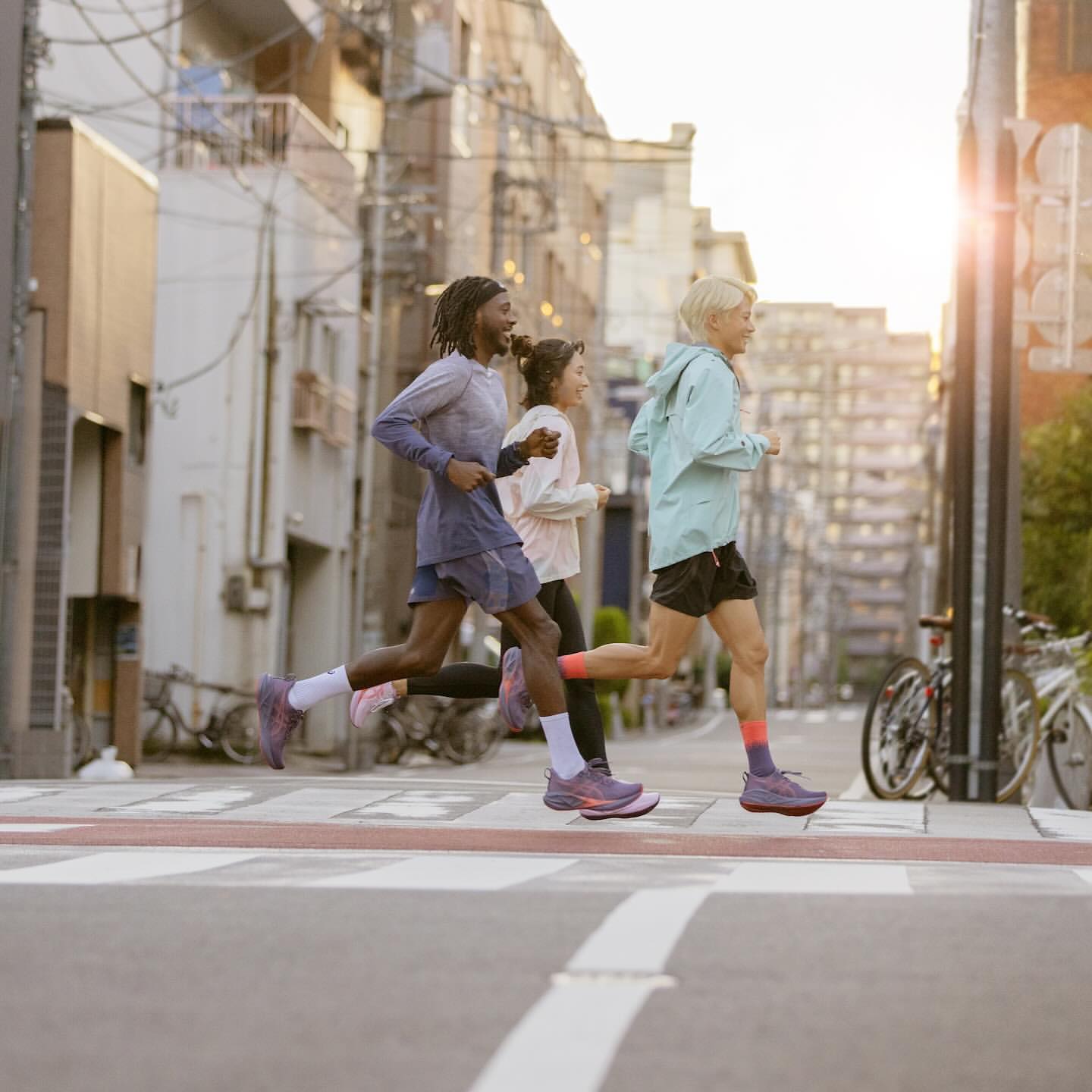 Three athletic people running in the street in athletic clothing and running shoes. Urban setting with buildings and street markings.
