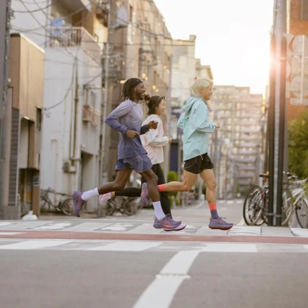 Three athletic people running in the street in athletic clothing and running shoes. Urban setting with buildings and street markings.