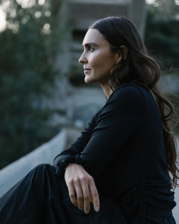 Profile portrait of a woman with long dark wavy hair wearing a black top outdoors in Los Angeles by photographer Adam Moran.