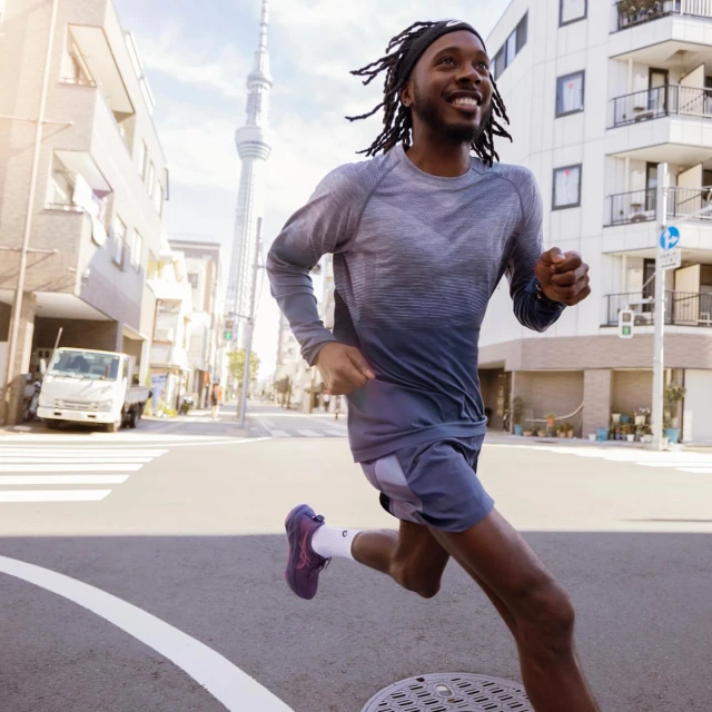 Athletic African-American man runs along a city street in workout gear with city buildings and tower in the background on a bright day.