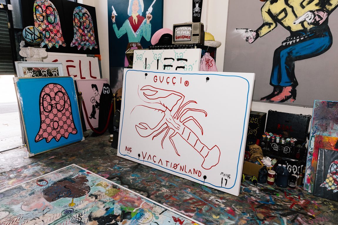 Indoor shot showcases assorted art canvases with drawings including Gucci logo, lobster, ghost, and cowboy designs in a creative workspace.