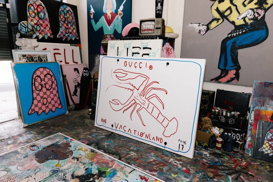 Indoor shot showcases assorted art canvases with drawings including Gucci logo, lobster, ghost, and cowboy designs in a creative workspace.