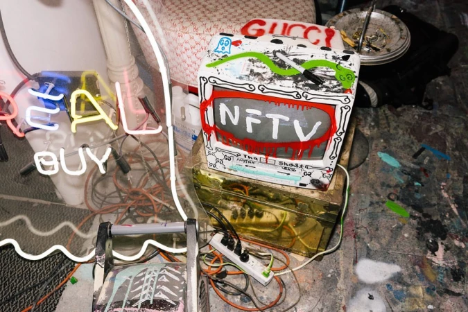 Vintage television set covered in graffiti art with the words 'NFTV' and 'Gucci' in an indoor, cluttered environment.