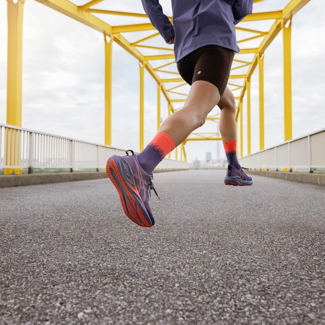 Person running across a yellow bridge wearing athletic shoes, shorts, and socks, with a cityscape visible in the distance.