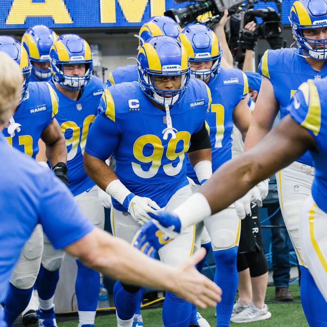 A group of American football players in blue and yellow uniforms walking onto the field, ready for a game, showcasing team spirit and energy.