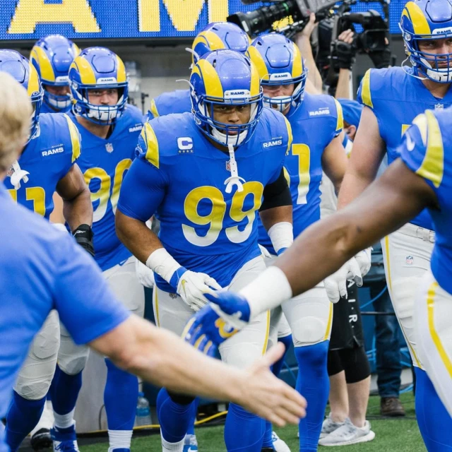A group of American football players in blue and yellow uniforms walking onto the field, ready for a game, showcasing team spirit and energy.