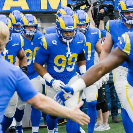 A group of American football players in blue and yellow uniforms walking onto the field, ready for a game, showcasing team spirit and energy.