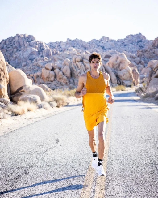 Athletic man in athletic wear running on a desert road with a backdrop of rock formations on a sunny day for fitness and health.