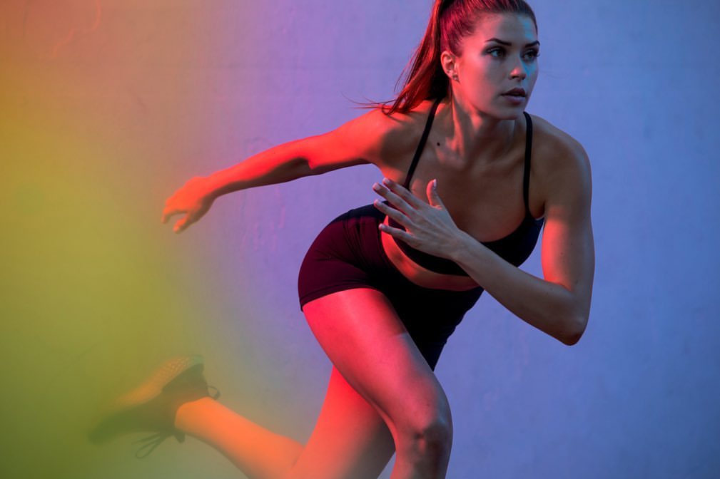 Woman in athletic wear sprinting with dynamic motion against a vibrant blue and red gradient studio backdrop.