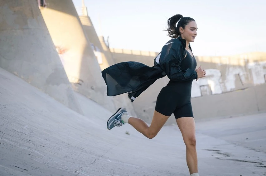 Athletic woman in activewear running in an urban environment with concrete walls and natural sunlight during the daytime.