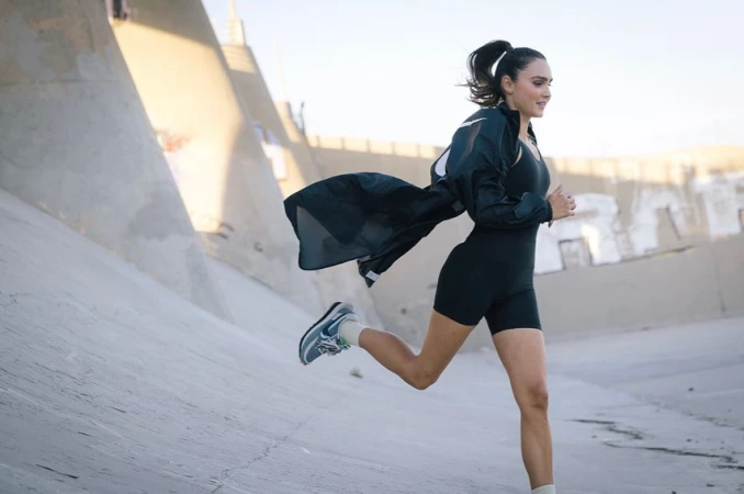 Athletic woman in activewear running in an urban environment with concrete walls and natural sunlight during the daytime.
