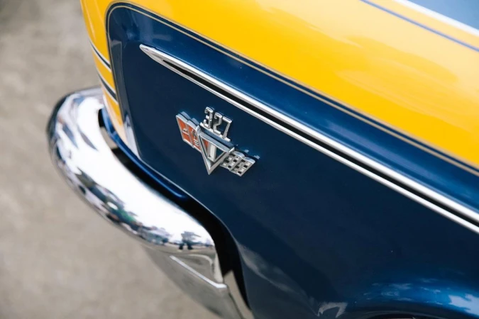 Close-up of a blue and yellow vintage car fender with a '327' emblem, showcasing classic automotive design details and chrome bumper.