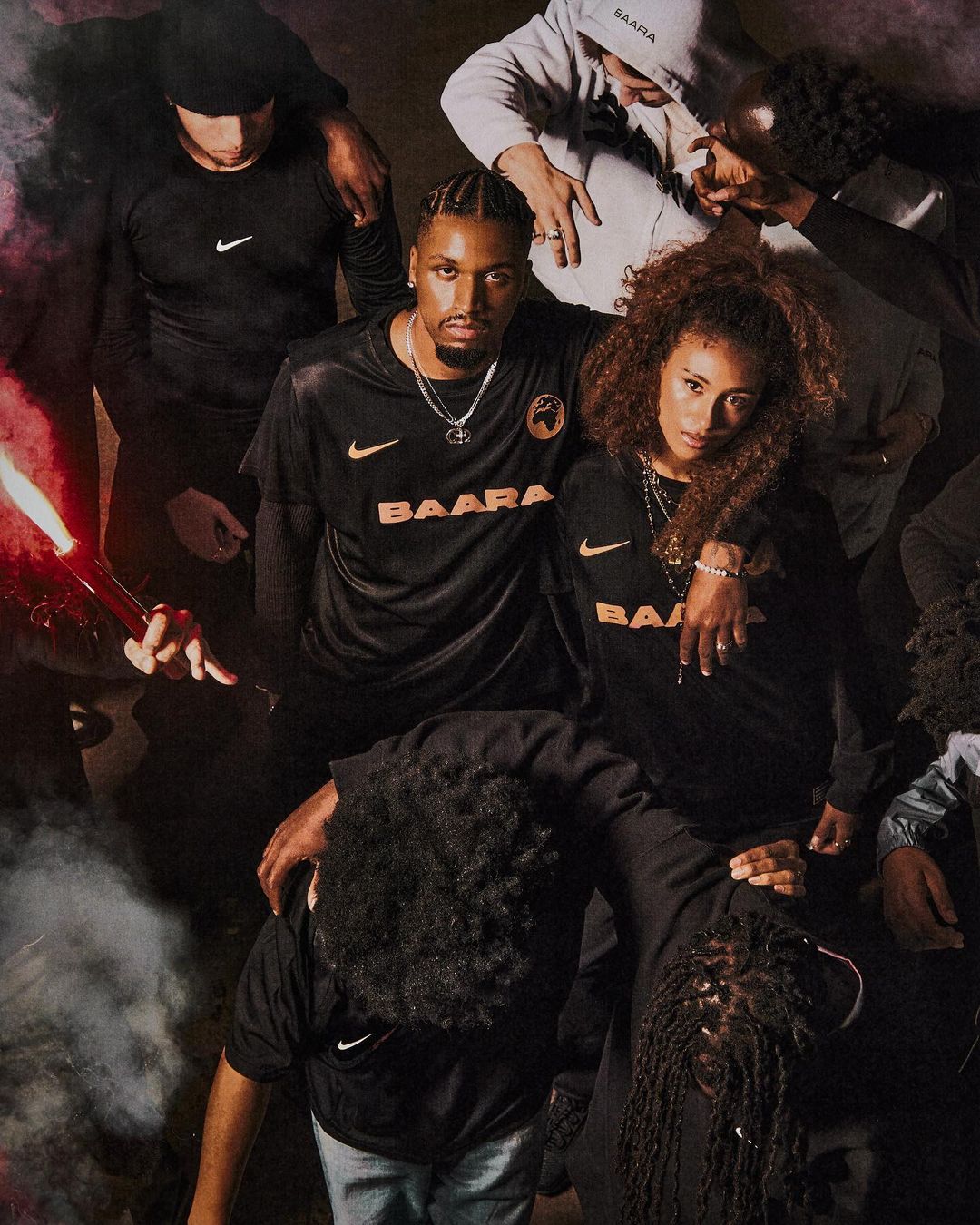 A group of diverse young adults wearing matching black sports jerseys with the word 'BAARA' in orange stand together indoors.