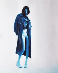 Model in long blue coat and white shorts standing against a light background by Adam Nestoret-puyon in Paris