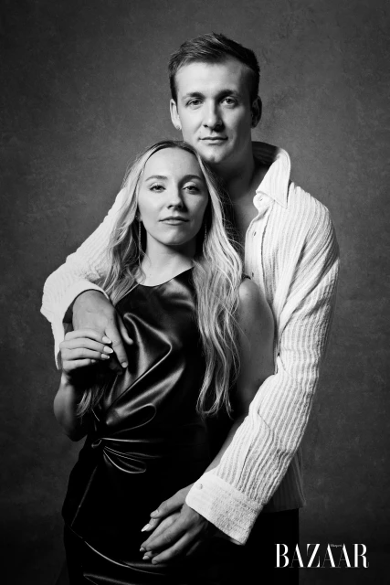 Black and white portrait of a couple embracing, with a woman in a black dress and a man in a white shirt against a mottled gray backdrop.