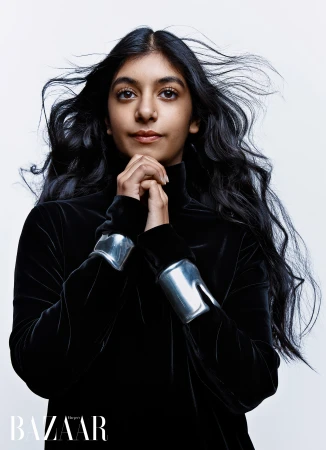 Model with windswept dark hair wearing a black velvet high-neck top and sculptural silver cuffs against a white background.