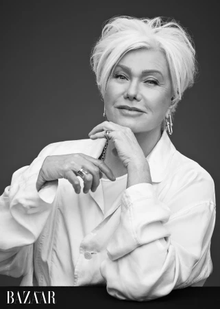 Black and white portrait of a woman with short white hair in a white collared shirt resting her chin on her hand.