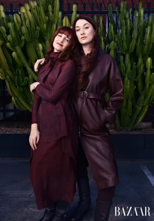 Two women posing together in burgundy outfits in front of a tall green cactus garden outdoors in Sydney.